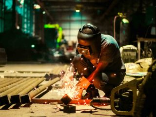 Worker grinding metal pipe ends, sparks flying in a dimly lit workshop
