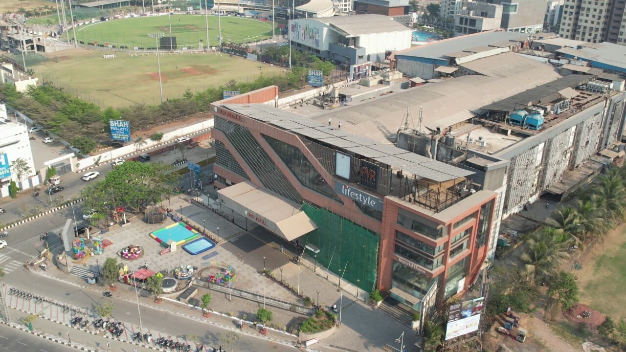 High-angle shot of rooftop solar panels on a Rahul Raj shopping mall with a sports field in background