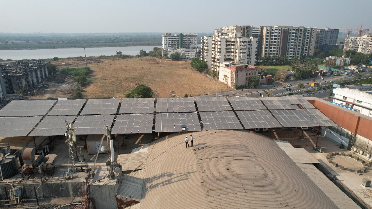 Technicians on a rooftop inspecting solar panels above an Rahul Raj commercial mall