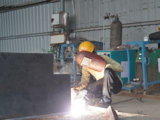 Welder wearing helmet and protective jacket performing a weld on a metal plate