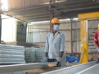 Worker in safety helmet and mask inspecting a steel beam inside the fabrication shop