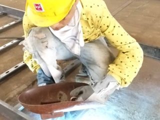 Worker in helmet and mask inspecting a small fabricated metal component