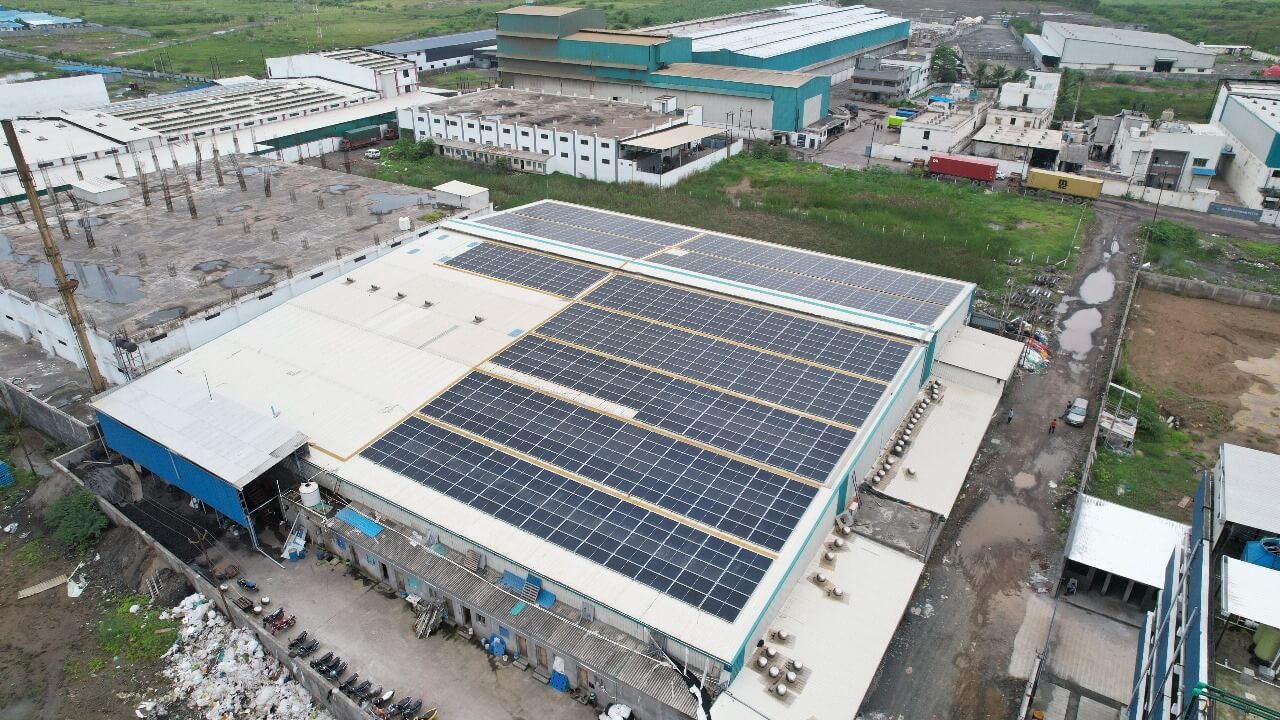 Wide-angle shot of solar panels covering an Nipun industrial warehouse roof with green fields beyond