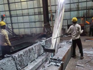 Two workers pulling a steel beam out of a hot-dip galvanizing tank