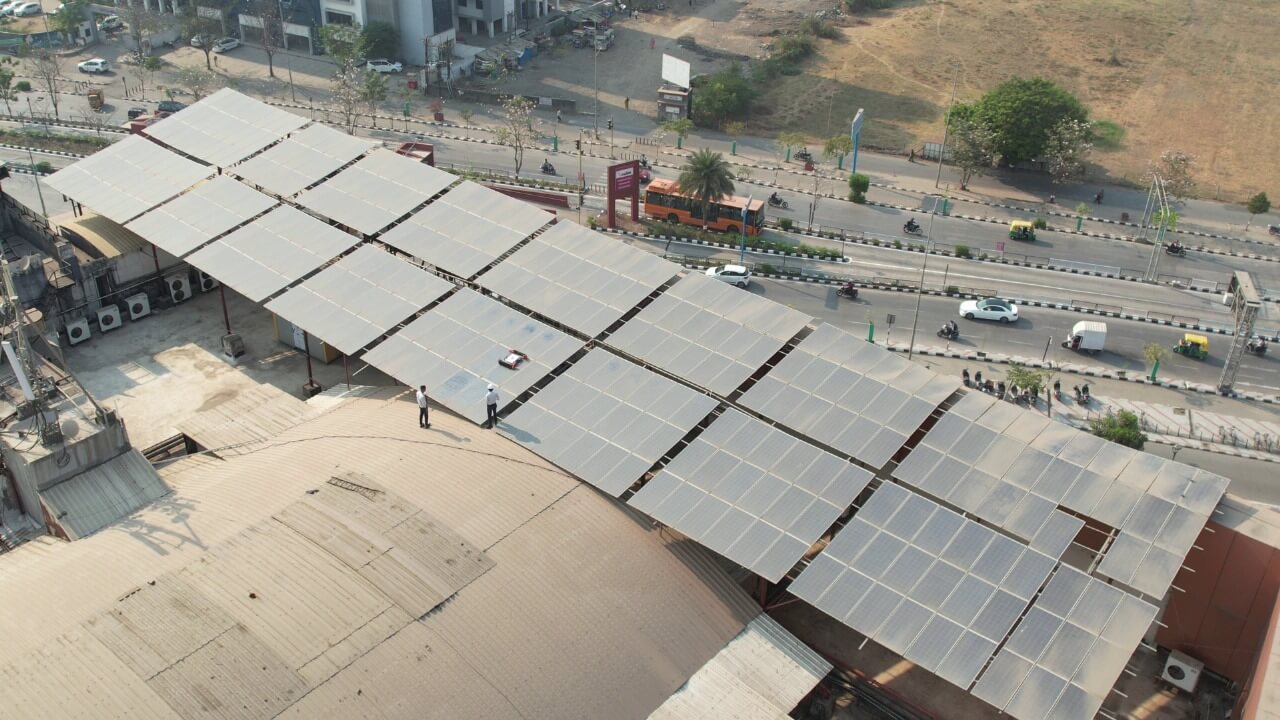 High-angle view of solar modules on an arched Rahul Raj commercial mall rooftop with urban road below