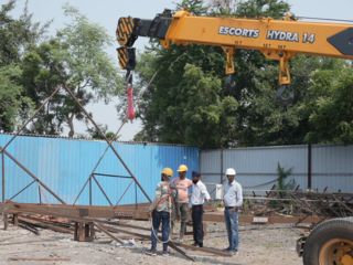 Mobile crane lifting a load as workers and supervisor observe in open yard