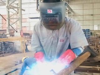 Close-up of a welder in gloves performing MIG welding on pipe