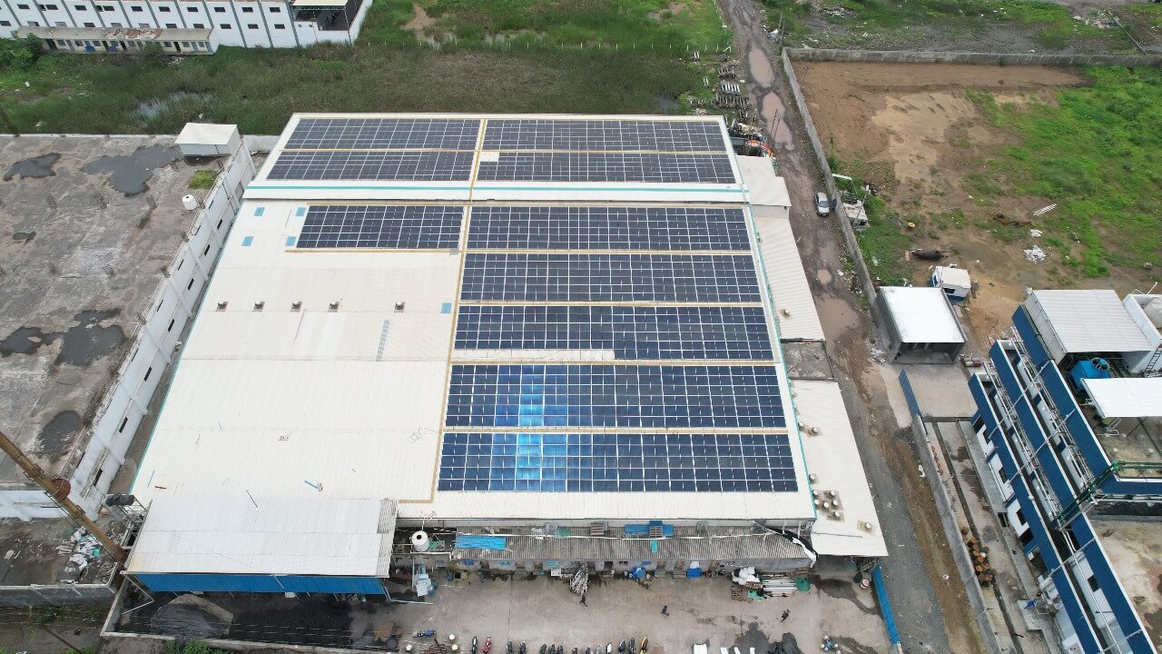 Top-down view of solar modules on a Nipun factory roof beside muddy service roads