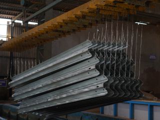 Rows of galvanized crash-barrier beams hanging on an overhead rack