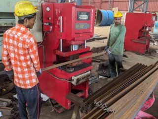 Two technicians feeding metal rods into a red hydraulic punching press